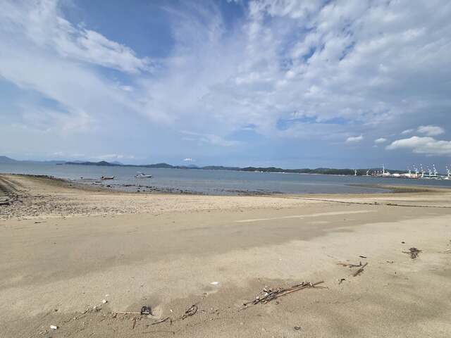 引き潮の広い砂浜。漁船と、その先に港が見える